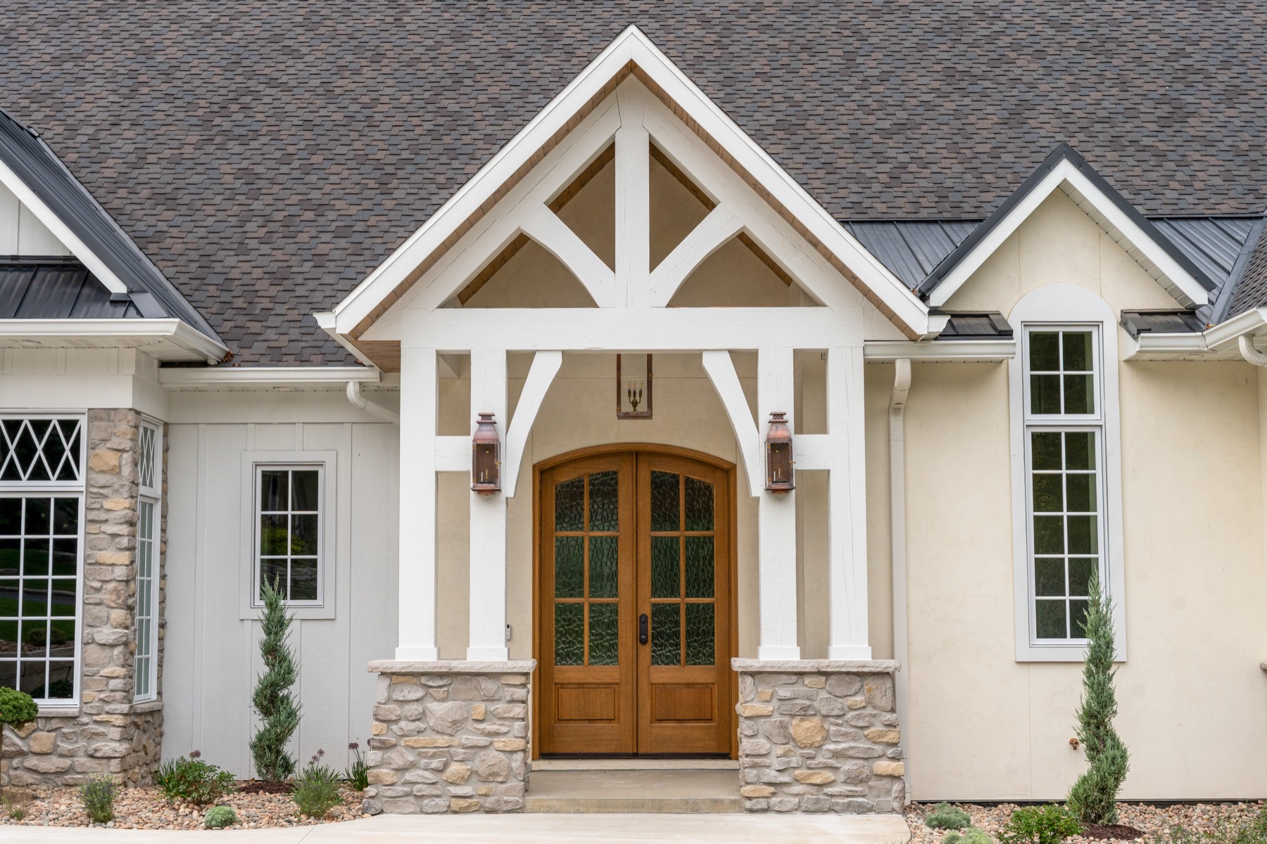 Craftsman home entry with timber gable, stone, and arched wood doors