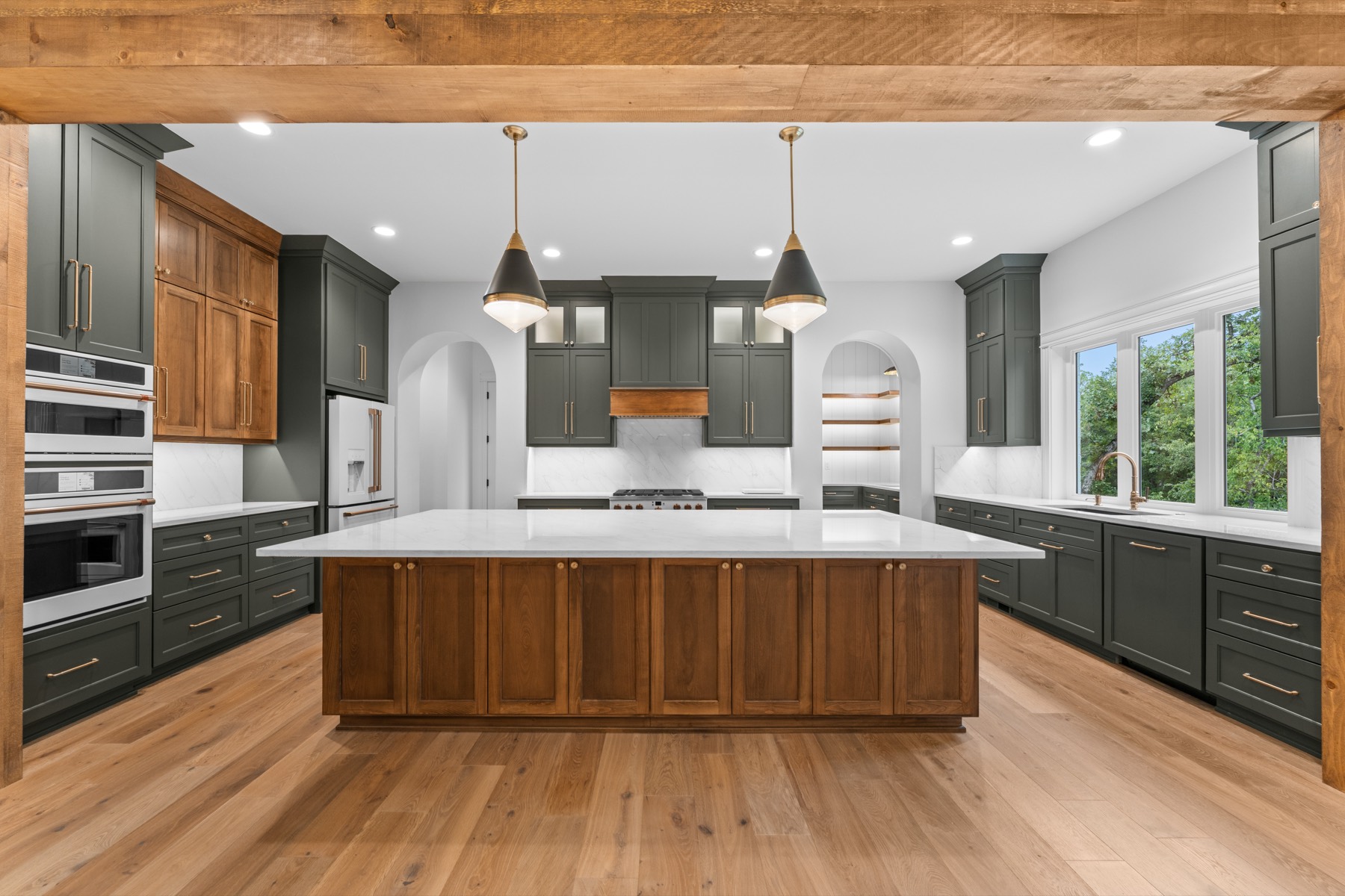 Kitchen with green cabinetry, a walnut island, and brass pendants